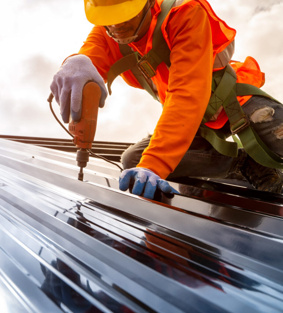 Construction worker installing new roof. Electric drill used on new roofs with Metal Sheet.