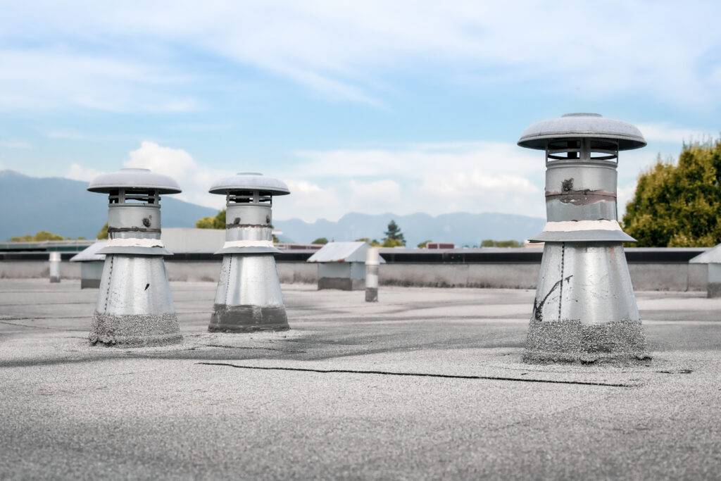 Flat roof vents on building with 2-ply SBS or modified bitumen roofing system. Group of metal ventilators such as: bathrooms and laundry exhaust and plumbing stack vent. Selective focus.